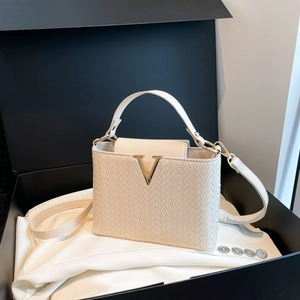 Petit sac carré beige à texture tissée avec boucle dorée en V dans un coffret cadeau