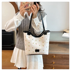 Close-up of white tote bag with pink rose patterns and black trim held by a model