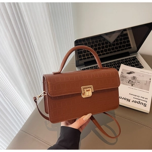 Detail of brown crocodile pattern handbag featuring a classic gold twist lock and handle