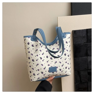 Detail of white leather tote bag featuring purple floral prints and light blue handle straps