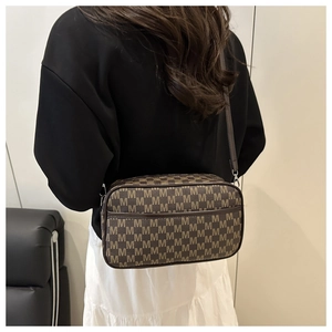 Detail of a brown crossbody bag with letter M patterns on a minimalist model shoot