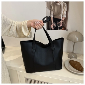 Detail of minimalist black faux leather tote bag held by a model in a French cafe setting