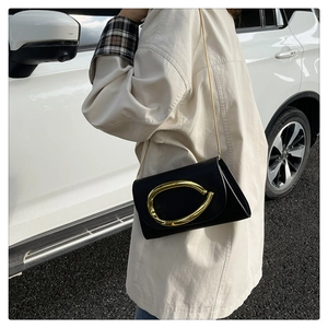 Close-up of black leather chain bag with large gold buckle on model with trench coat