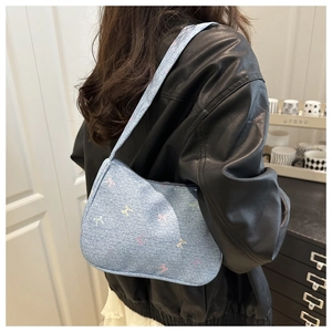 Side view of a light blue denim shoulder bag with colorful bow embroidery worn by a model