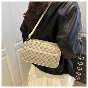 Vue détaillée d'un sac bandoulière avec imprimé monogramme M gris sur surface crème