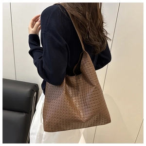Détail de la texture tressée du cabas en cuir marron foncé et de sa large bandoulière