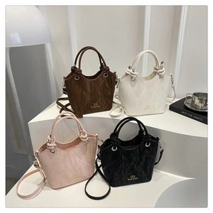 Collection of textured bucket bags in brown, white, pink, and black on geometric stands