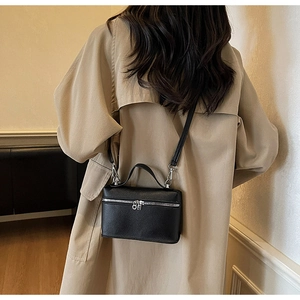 Détail d'un petit sac carré noir porté sur un trench-coat beige élégant et moderne