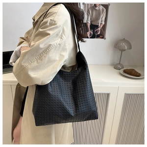 Détail d'un grand sac cabas noir en cuir tressé porté par un mannequin en trench-coat