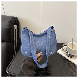 Detail of blue denim underarm bag featuring pink bow embroidery and wide canvas strap