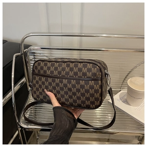 Détail d'un sac bandoulière marron avec imprimé lettre M et bandoulière réglable