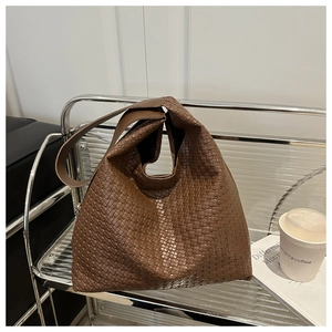 Détail d'un sac hobo tressé marron foncé sur une étagère en métal avec une tasse à café