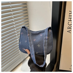 Detail of blue denim underarm bag featuring colorful pastel bow prints and wide strap