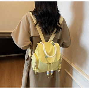 Detail eines gelben Nylonrucksacks mit blauem AI-Logo, Kordelzügen und bunten Perlen