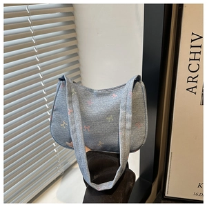 Detail of light blue denim shoulder bag featuring colorful all-over bow embroidery pattern
