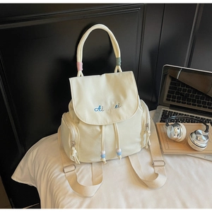 Detail of cream drawstring backpack showing embroidered logo and colorful bead accents