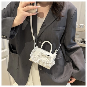 Mini white leather crossbody bag with lace edges and bow detail worn with grey suit