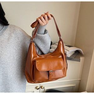 Caramel brown patent leather hobo bag with front pocket shown held by a model
