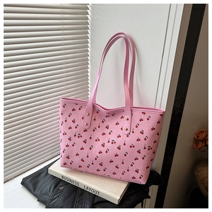 Gros plan du sac cabas rose à imprimé cerises et rivets dorés posé sur des livres