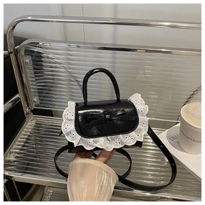 Detail of black patent leather mini handbag with white lace trim and bow on metal chair