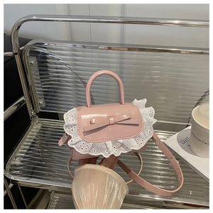 Detail of pink mini handbag with lace edges, ribbon bow, and top handle on a sleek stand