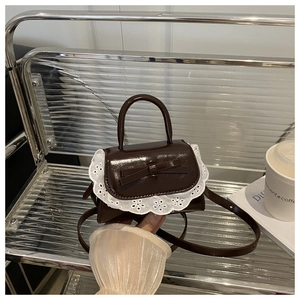 Detail of sweet lace trim and bow on dark brown patent leather crossbody handbag