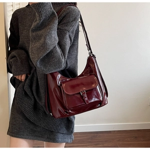 Model wearing dark burgundy crescent hobo bag with glossy finish and buckle detail