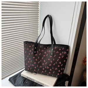 Détail d'un sac cabas noir avec imprimés cerises rouges sous une lumière naturelle