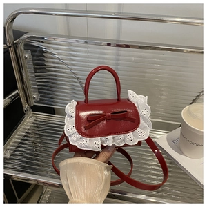Close-up of a mini red bow handbag with elegant white lace trim and adjustable strap