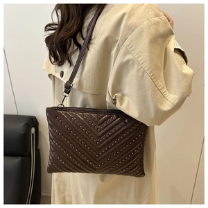 Detail of dark brown faux leather crossbody bag with silver V-shaped stud accents