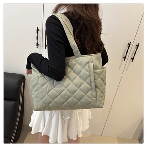 Detailed view of spacious green quilted tote bag with diamond stitching on a model
