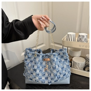 Detail view of light blue checkerboard denim tote with fringe edges and gold deer charm