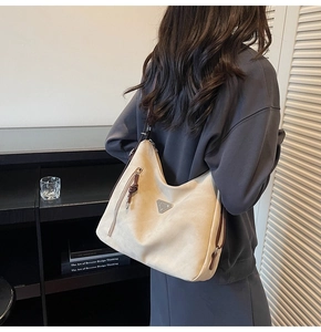 Detail of off-white tote bag featuring silver triangular logo and brown leather zipper pull
