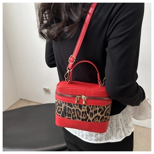 Detail view of red leather cylinder bag with leopard print stitching and gold metal zipper
