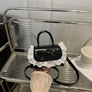 Fashionable black patent leather bow handbag with white lace trim and crossbody strap