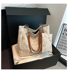 Close-up of cream tote bag set with brown straps and chain detail inside a gift box