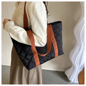 Macro shot of black quilted tote bag featuring vibrant orange woven shoulder straps