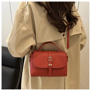 Close-up of red litchi texture handbag with gold buckle held by a model in a beige coat