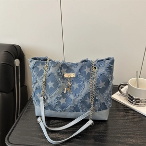 Denim tote bag with star pattern, chain strap and deer pendant on a black surface