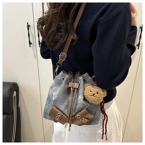 Detail of washed denim bucket bag featuring leather trim, drawstring, and bear charm