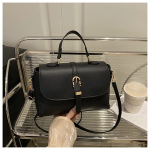 Détail d'un sac à bandoulière en cuir noir avec boucle dorée et poignée sur l'étagère