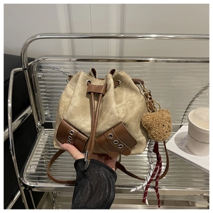 Detail of khaki canvas drawstring bucket bag with brown leather trim and bear pendant