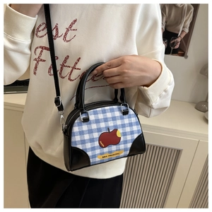 Detail of blue plaid crossbody bag with red apple patch and leather handles on model