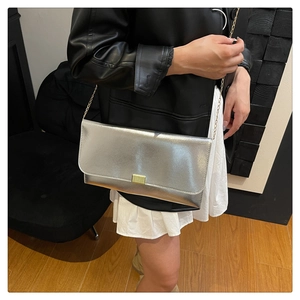 Close-up of silver textured envelope bag with gold chain strap on black leather jacket
