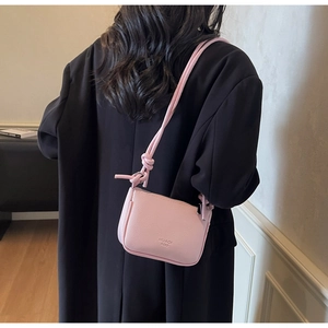 Close-up of a light pink lychee leather crossbody bag with embossed logo on back of model