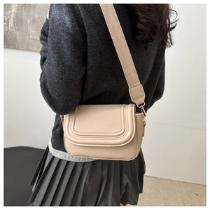 Model wearing a beige saddle bag with wide strap and curved stitching on the flap