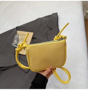 Detail of yellow pebbled leather crossbody bag with knot strap and silver zipper closure