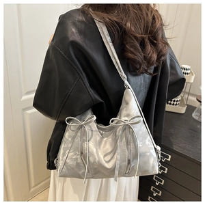 Detail view of silver metallic hobo bag with bows and zippers on model back