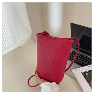 Detail der roten Eimertasche mit Lychee-Muster und Logoprägung vor modernem Schreibtisch