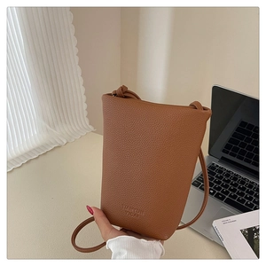 Detail der braunen Eimertasche mit Kieselleder-Struktur, Logo-Prägung und Schultergurt